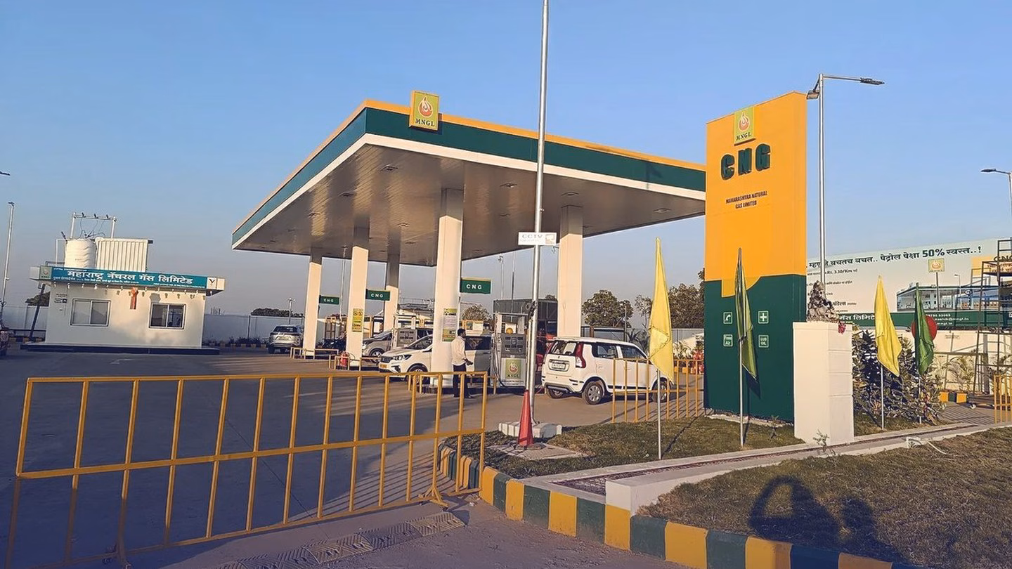 A CNG filling station forecourt in Maharashtra: a canopy over the dispensers, a tall CNG sign and parked cars under a clear sky.