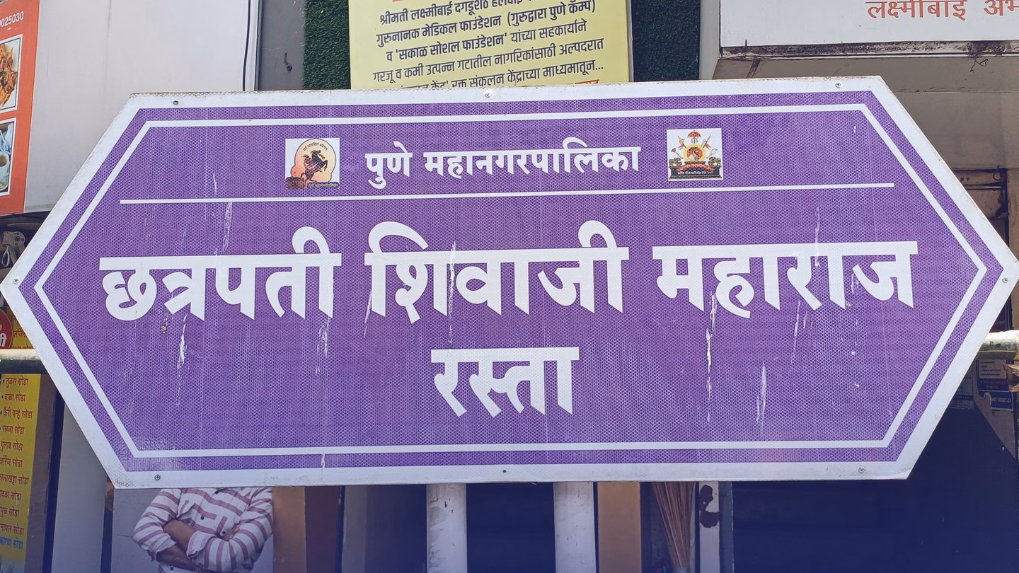 A purple Pune Municipal Corporation street sign in Marathi reading छत्रपती शिवाजी महाराज रस्ता.