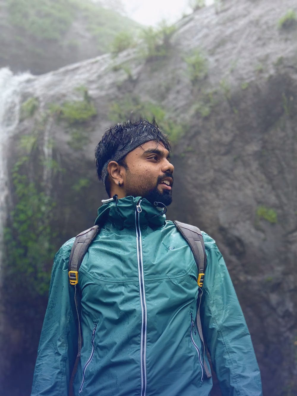 Abhinav in a rain jacket and headband in front of a waterfall on a monsoon trek near Naneghat.