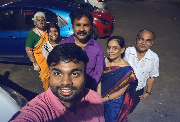 Abhinav takes a selfie with six family members of three generations, beside parked cars.