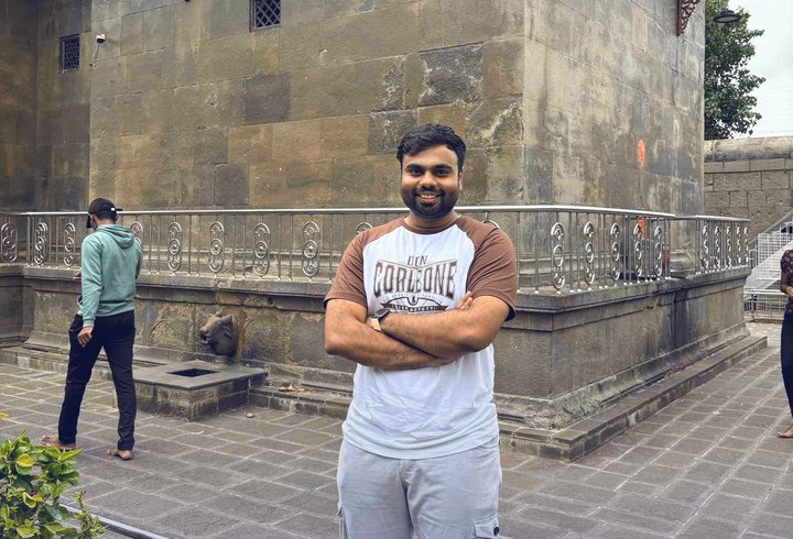 Abhinav standing with his arms folded in front of an old stone building.