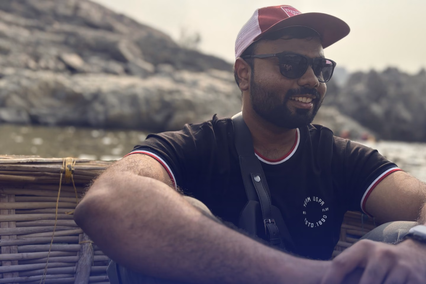 Abhinav sitting in a round woven coracle on the Tungabhadra river, with rocks behind him.