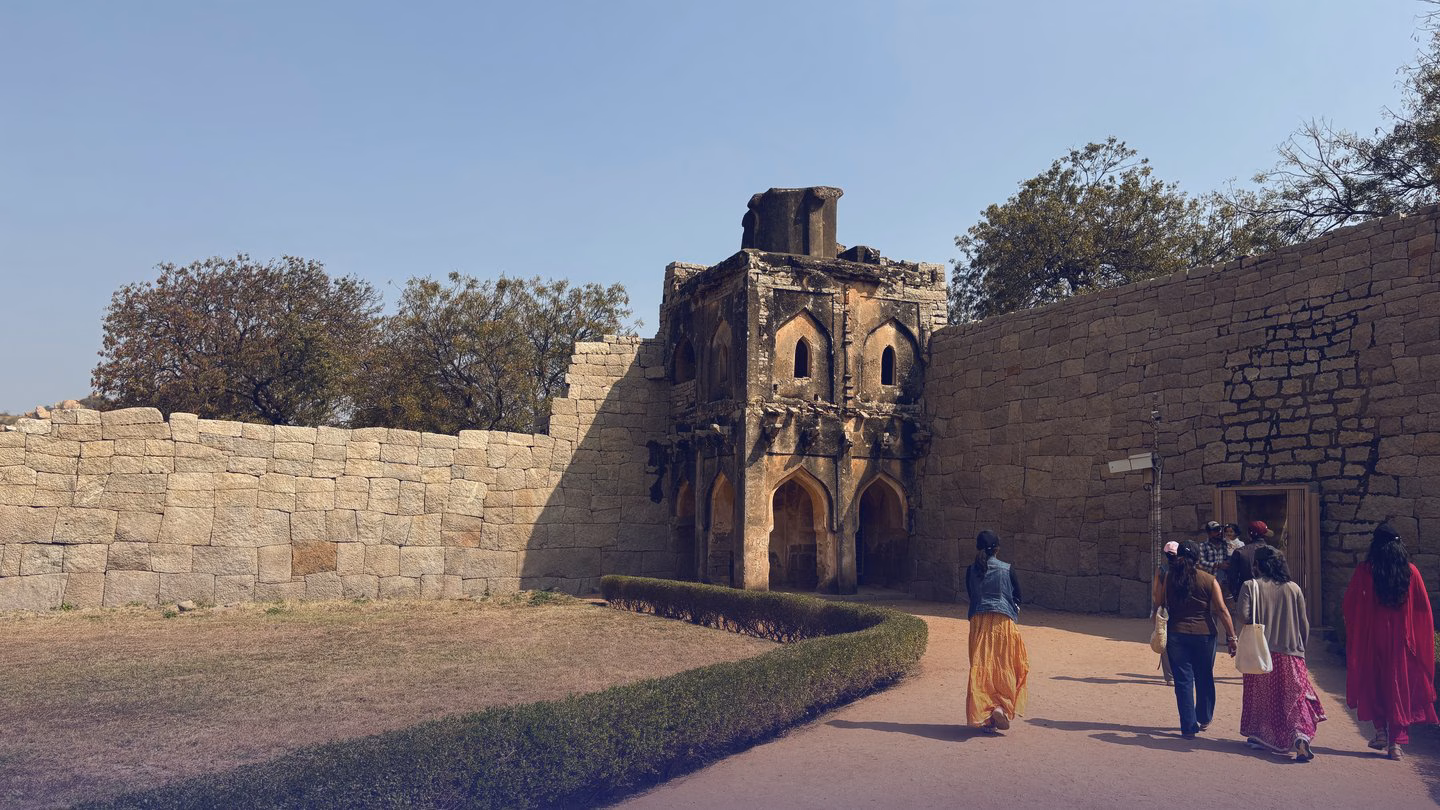The high stone walls of the Queen's Bath in Hampi, with a garden path along them.