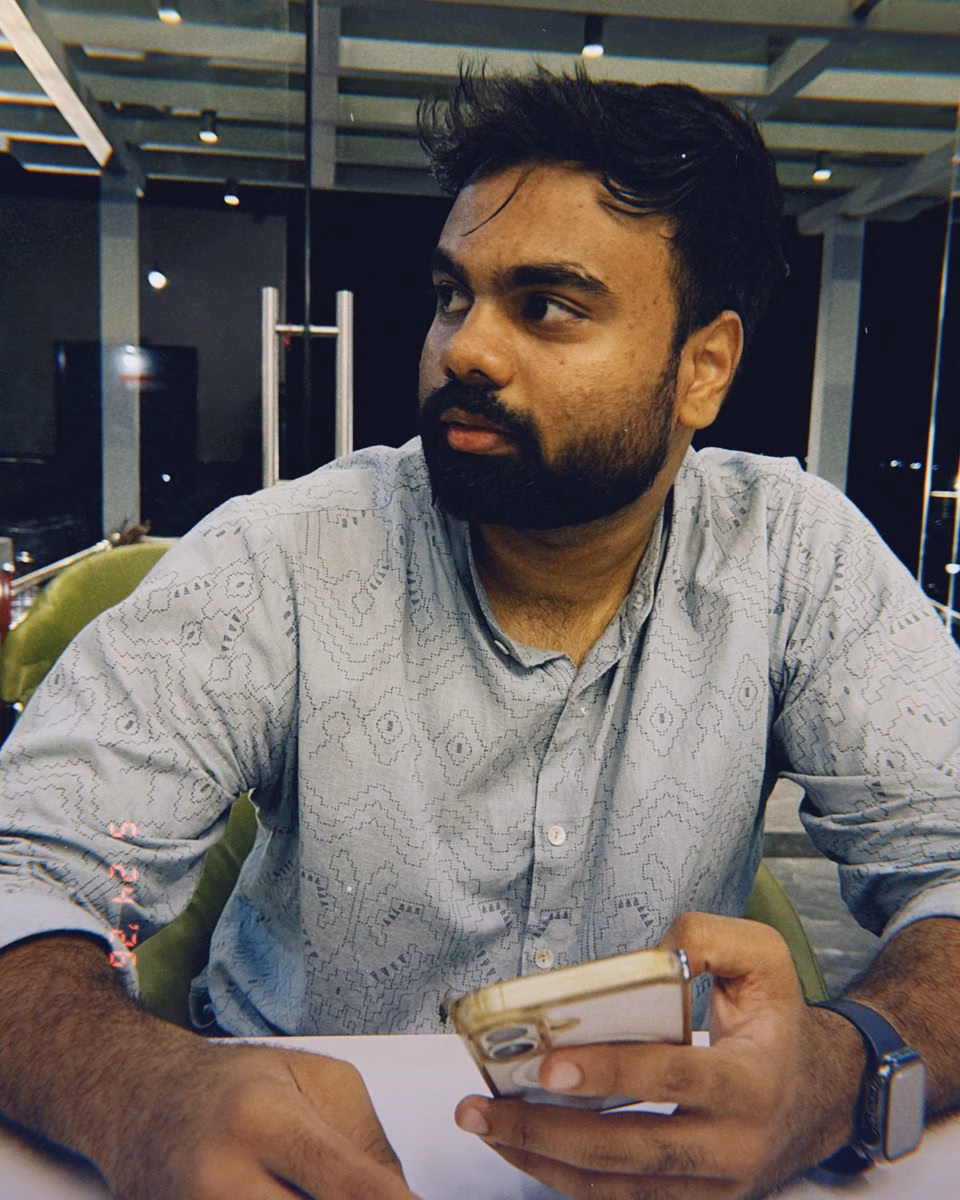 Abhinav at a café table in the evening, phone in hand, looking up.